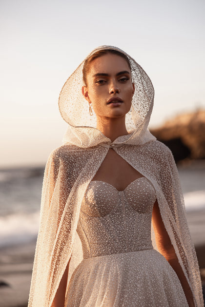 Close-up of Amira’s hooded cape shows soft tulle and a clean, refined hem that lends elegant finishing.