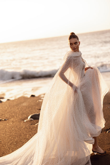 The airy tulle hooded cape for Amira can be taken off after the ceremony, offering a romantic and dramatic detail.