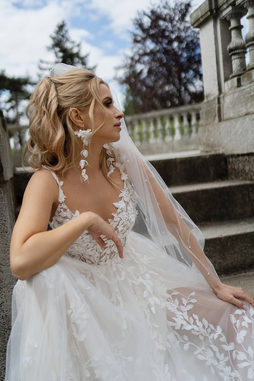 Seated bride on outdoor steps, Regular pearl veil falling behind her back in profile