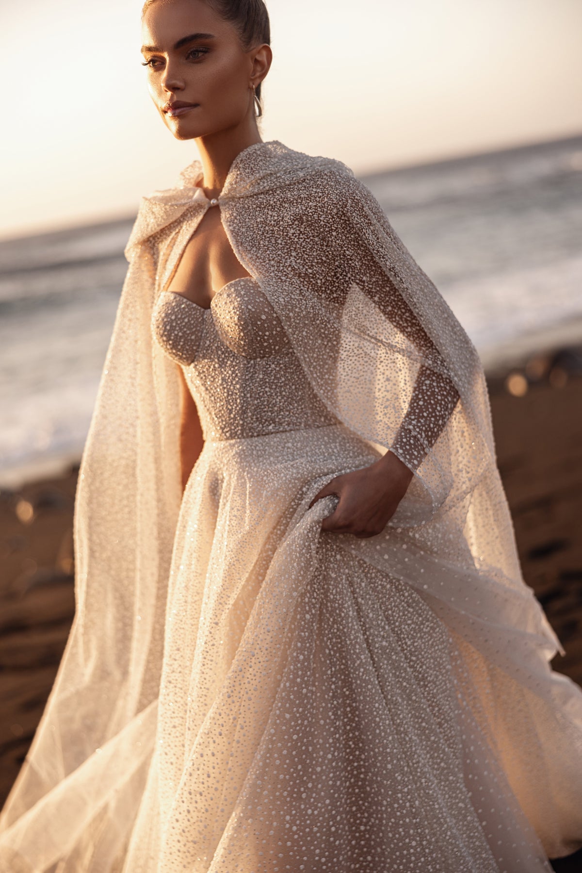 Amira bridal cape in sheer embellished tulle gracefully enhances the silhouette of the wedding gown.