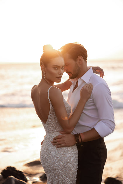 Beaded lace wedding dress with an open back and intricate pearl embellishments, captured at sunset.