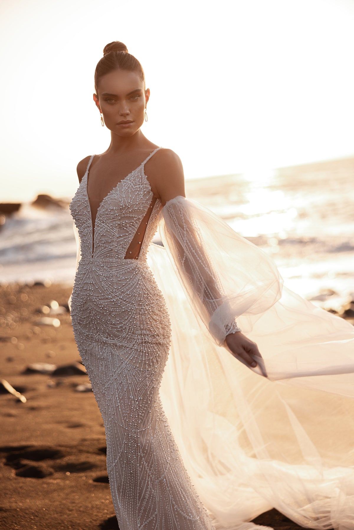 Beaded wedding dress with plunging V-neckline, pearl detailing, and sheer puff sleeves for a modern bridal look.
