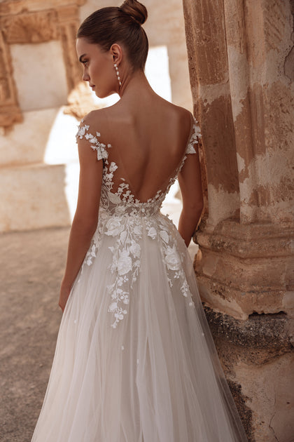 The Andrea wedding dress with an open back and long flowing train embodies ethereal elegance and modern romance.