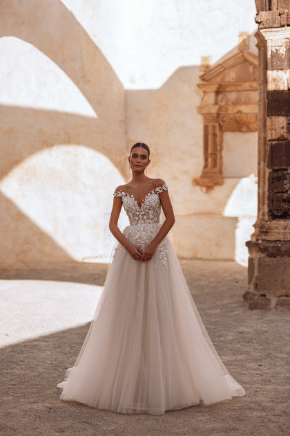 The Andrea wedding gown with an open back and lace bodice creates a stunning silhouette with a soft tulle train.