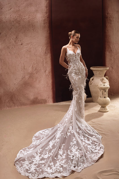 The Aspasia mermaid wedding dress with lace appliqués and feather details enhances feminine curves with couture glamour.