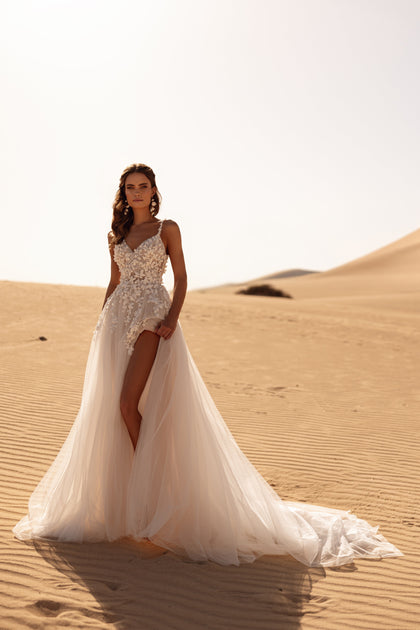 The Aviva wedding dress with a long train and flowing veil creates a breathtaking bridal look in the golden desert light.