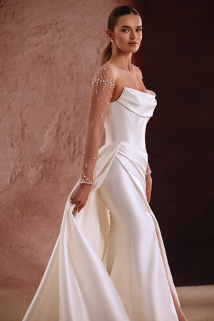 The Aylin wedding dress features pearl-embellished sheer sleeves and a draped satin neckline for a timeless bridal look.
