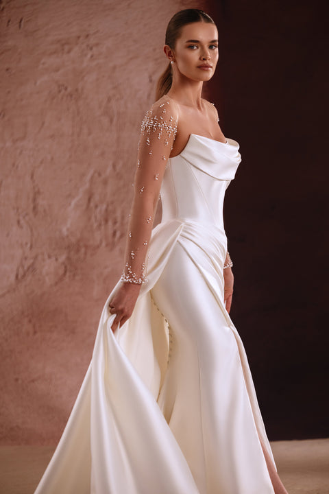 The Aylin wedding dress features pearl-embellished sheer sleeves and a draped satin neckline for a timeless bridal look.