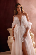 The Bella wedding dress features an off-the-shoulder corset bodice and tulle floral appliqués, creating a romantic princess bridal look.