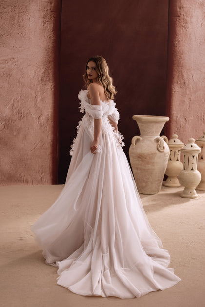 The Bella wedding dress with off-the-shoulder sleeves and flowing tulle train offers a dreamy and romantic bridal silhouette.