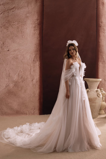 The back of the Bella wedding gown reveals a sweeping tulle train adorned with 3D flowers for a fairytale bridal look.