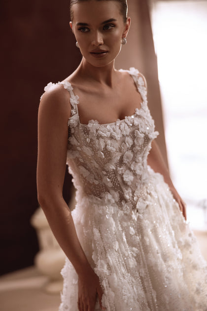 The Cintra wedding gown features a lace-up back and flowing train, creating a fairy-tale silhouette full of romance.