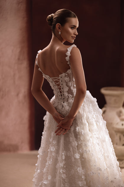 The Cintra wedding dress showcases a sheer lace bodice adorned with floral appliqués for a sophisticated, romantic style.