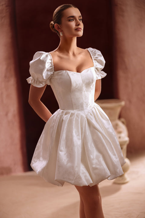 The Daphne short wedding dress features puff sleeves and a corset bodice, combining vintage charm with modern bridal chic.