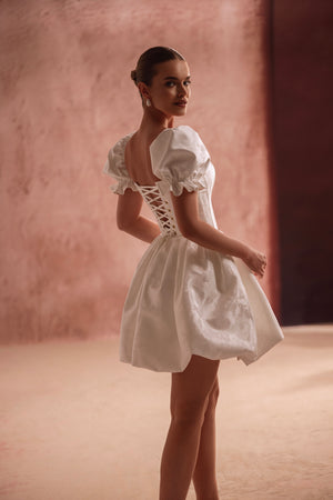 The Daphne wedding mini dress with lace-up corset back and puff sleeves highlights the waist, offering a flirty princess look.