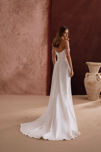 The Eleonore wedding dress with off-the-shoulder neckline and soft ruching radiates timeless beauty and pearl-accented charm.