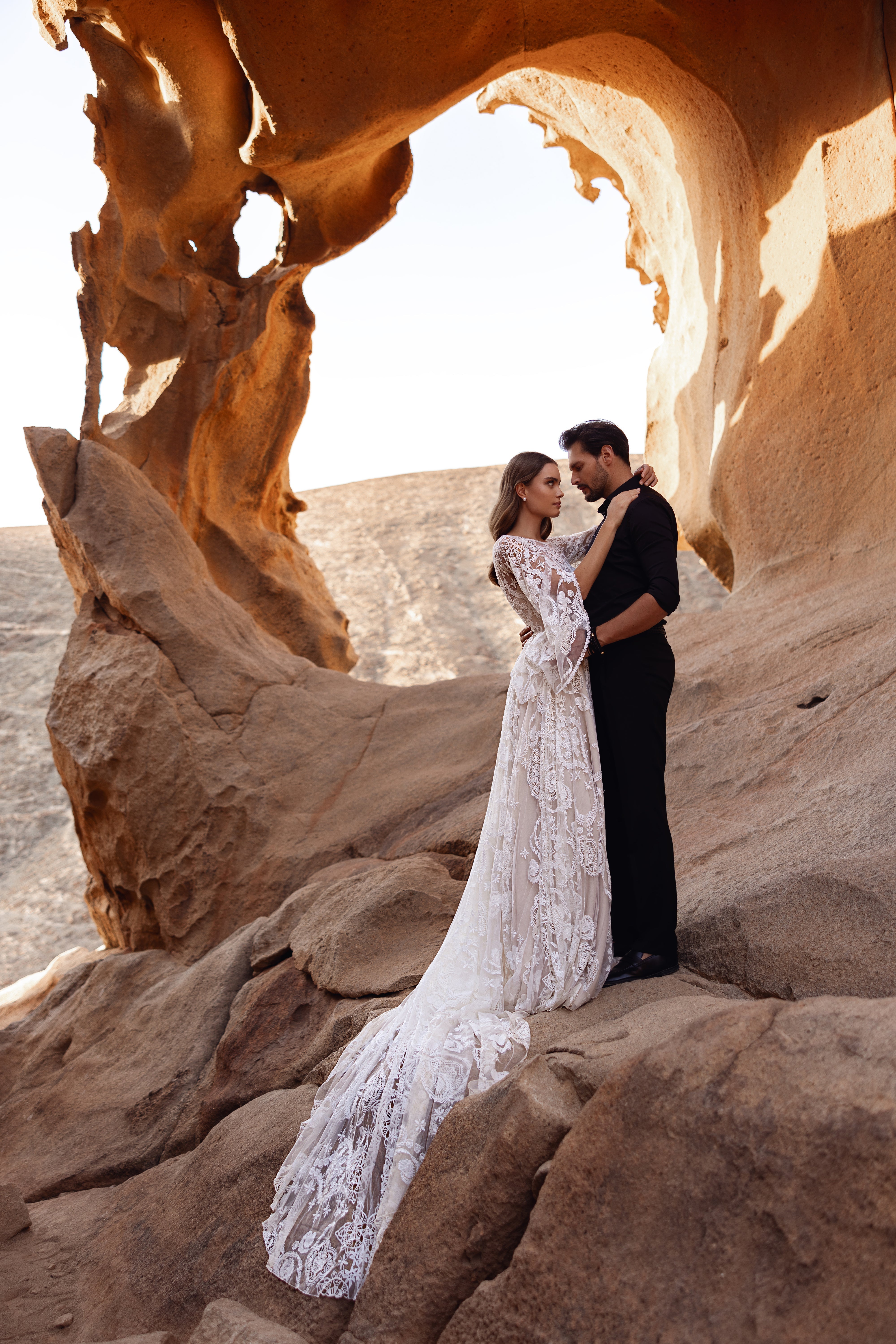 The Dune wedding dress features a sheer lace bodice and bell sleeves with intricate floral embroidery for a romantic boho look.