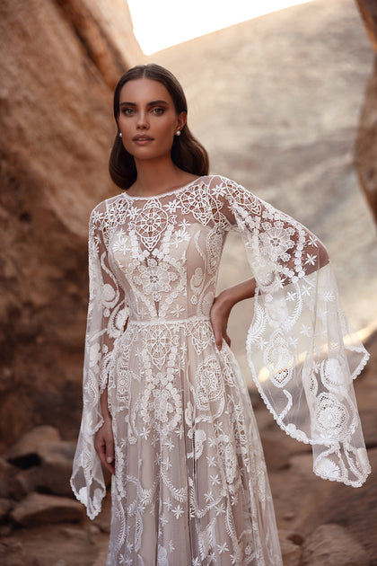 The Dune wedding dress features a dramatic lace train and flared sleeves, perfect for a boho-chic desert bride.