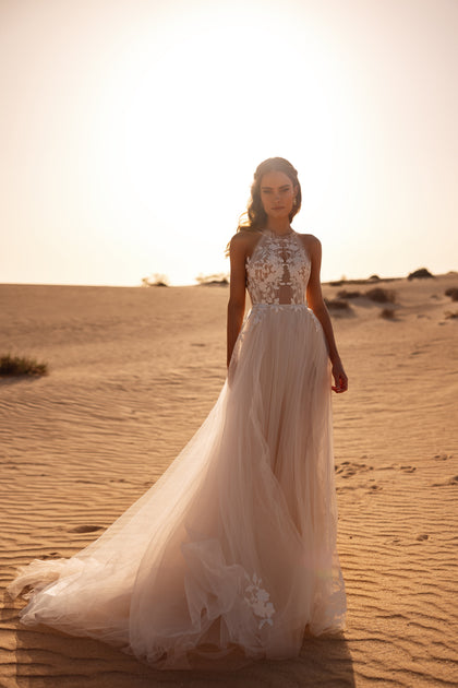The Ellie wedding dress features an illusion halter bodice and flowing tulle skirt adorned with floral appliqués for a romantic bridal look.