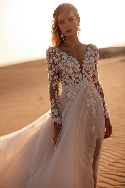 The Farida wedding dress features a deep V-neckline, long lace sleeves, and delicate 3D floral appliqués for a romantic bridal look.