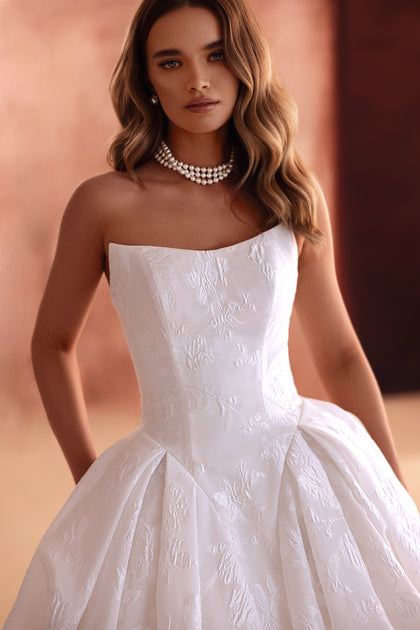 The Hebe wedding dress features a strapless ball gown silhouette with floral jacquard fabric, perfect for a timeless bridal look.