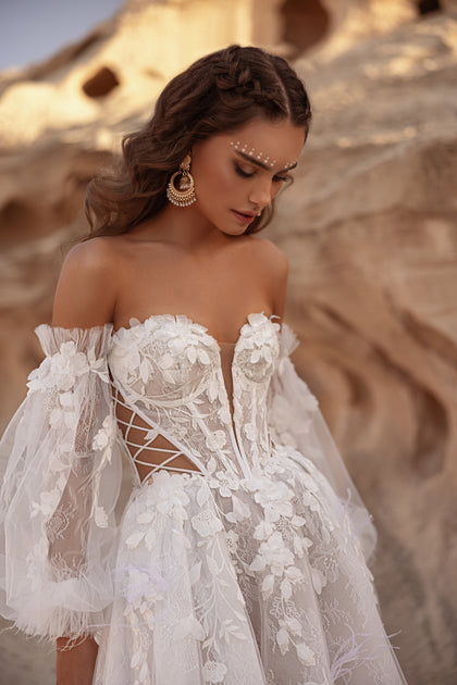 The Huda wedding gown features off-the-shoulder sleeves and a structured lace corset for a modern boho glamour look.