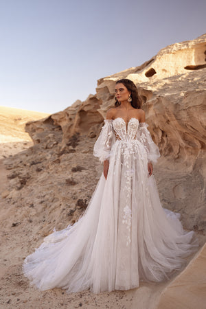 The Huda wedding dress features an off-the-shoulder corset with 3D floral appliqués and side lacing for a modern boho bridal look.
