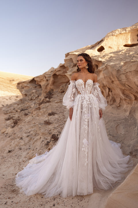 The Huda wedding dress features an off-the-shoulder corset with 3D floral appliqués and side lacing for a modern boho bridal look.