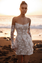 The Kayla wedding dress features off-the-shoulder sleeves and intricate 3D floral embroidery, perfect for a romantic beach wedding.