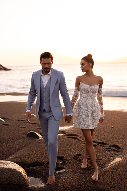 The Kayla short wedding dress with sheer long sleeves and 3D floral appliqués offers a modern twist on timeless bridal style.