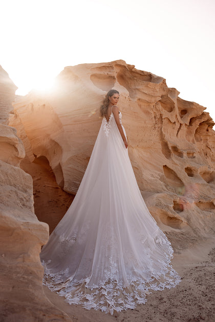 The Malika wedding gown with a long flowing train creates a stunning bridal look in a desert landscape.