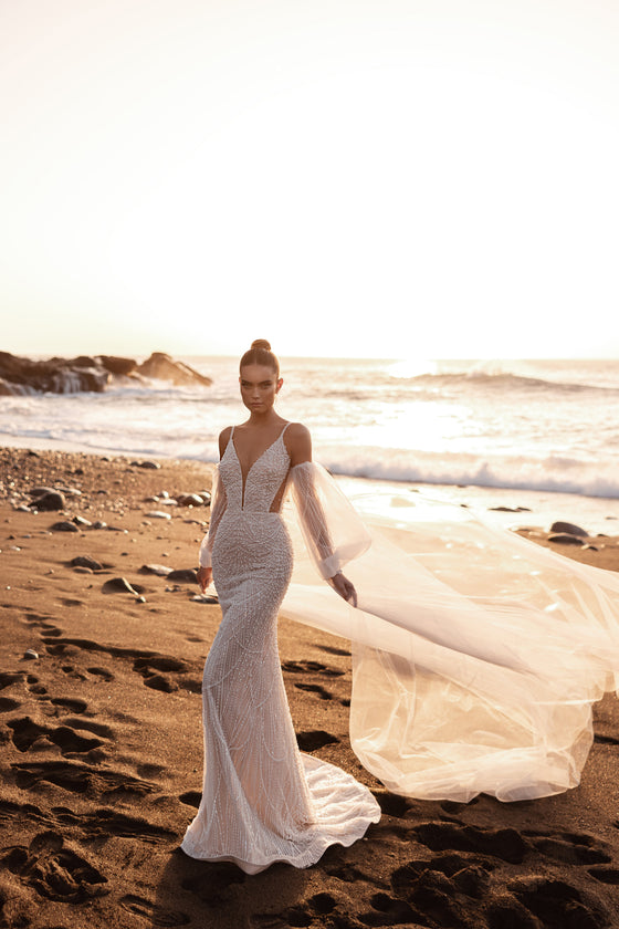 Fitted mermaid wedding dress with a deep V-neckline and flowing chapel-length veil on the beach.