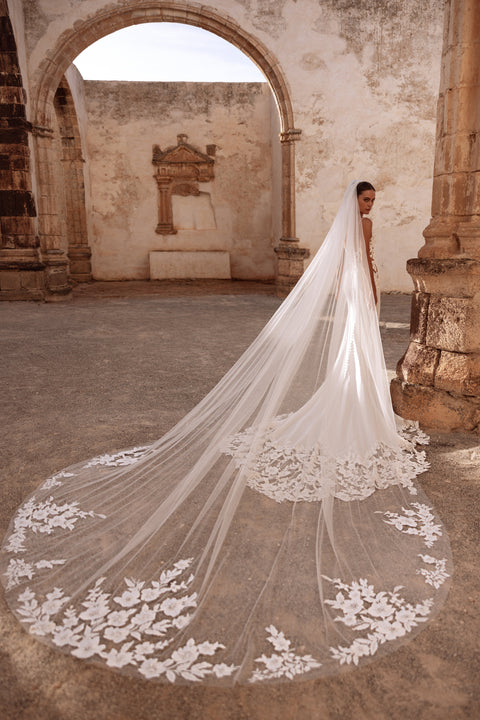 Munira cathedral wedding veil with floral lace appliqués, creating a dramatic bridal look in historic ruins.