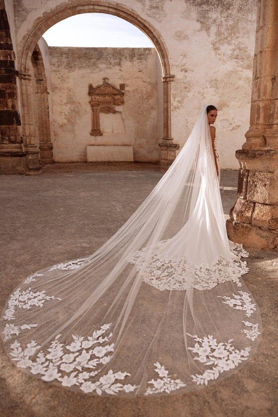 Munira cathedral wedding veil with floral lace appliqués, creating a dramatic bridal look in historic ruins.