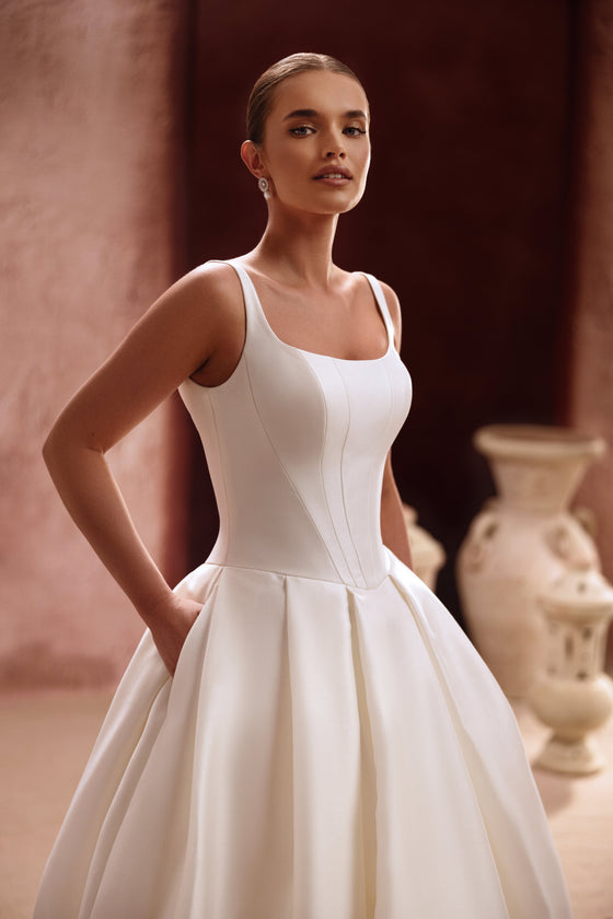 The Nicolette wedding dress features a clean satin bodice with straps and a voluminous princess skirt for a timeless bridal look.