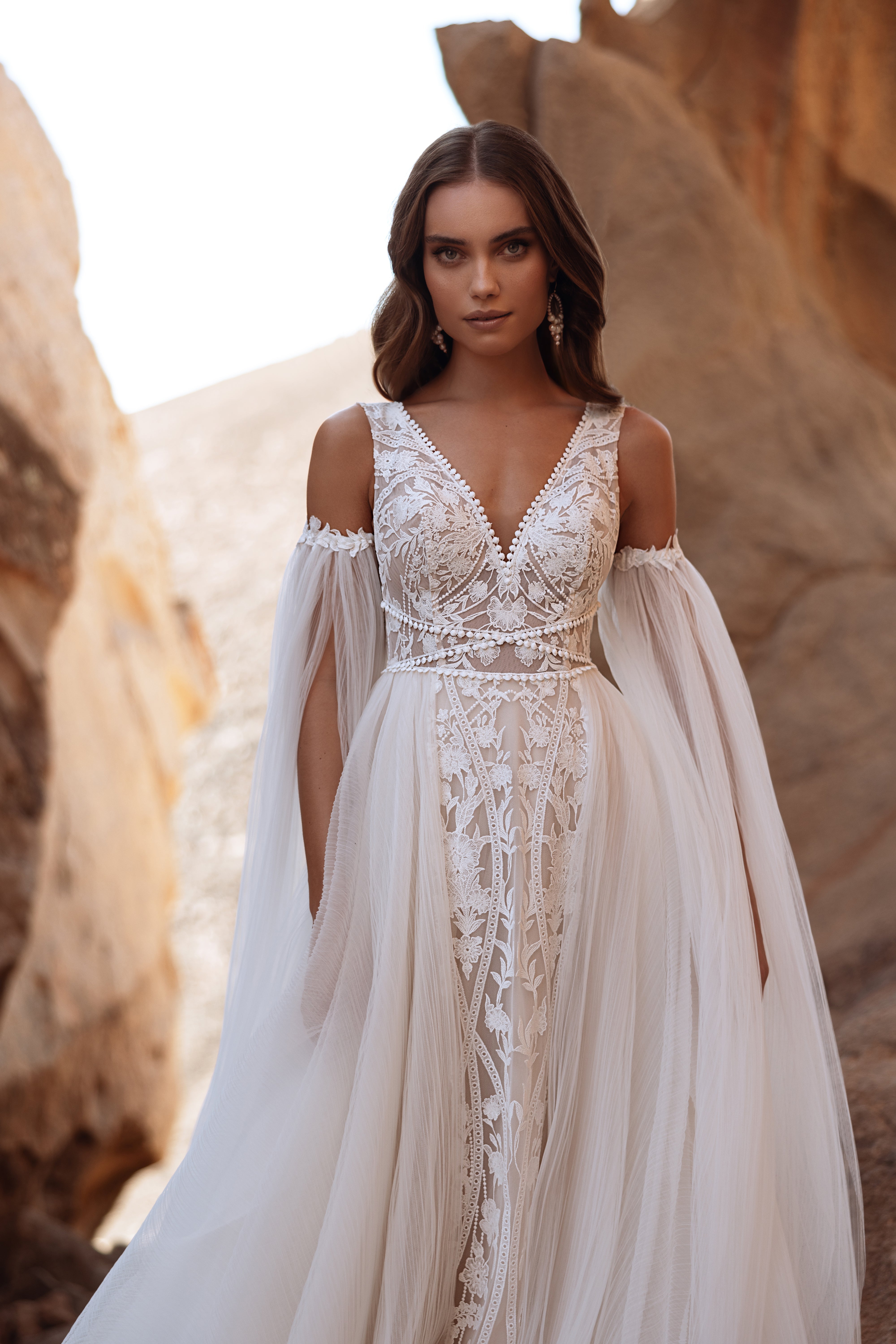 The Salome off-the-shoulder wedding dress with long tulle sleeves blends boho charm with romantic lace detailing.