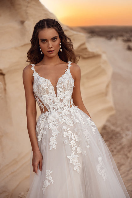 The Zafira wedding dress with a tulle skirt and floral lace details, paired with a groom in a beige suit, creates a dreamy bridal look.
