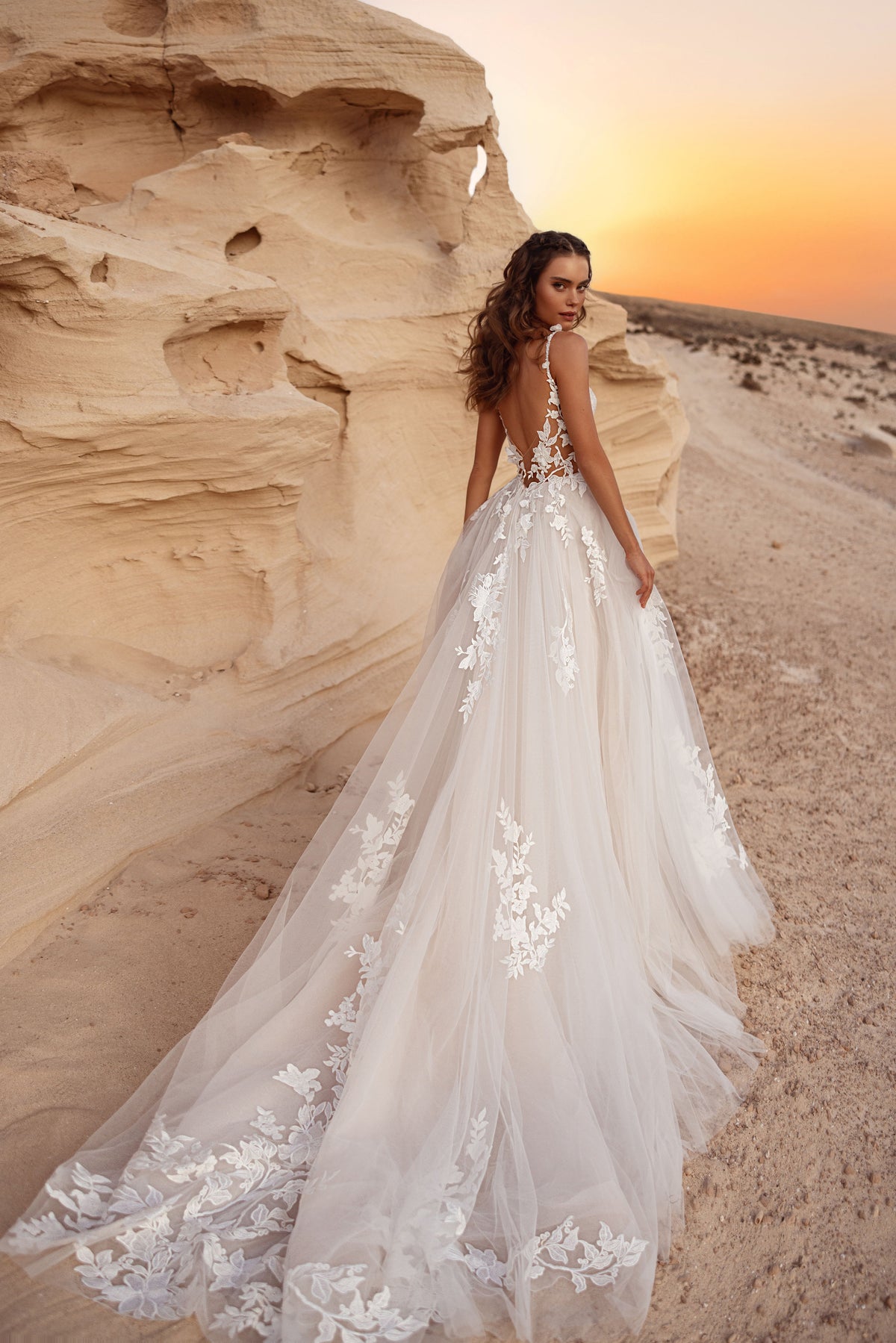 The Zafira wedding dress with an open back and a long tulle train adorned with 3D floral lace appliqués.